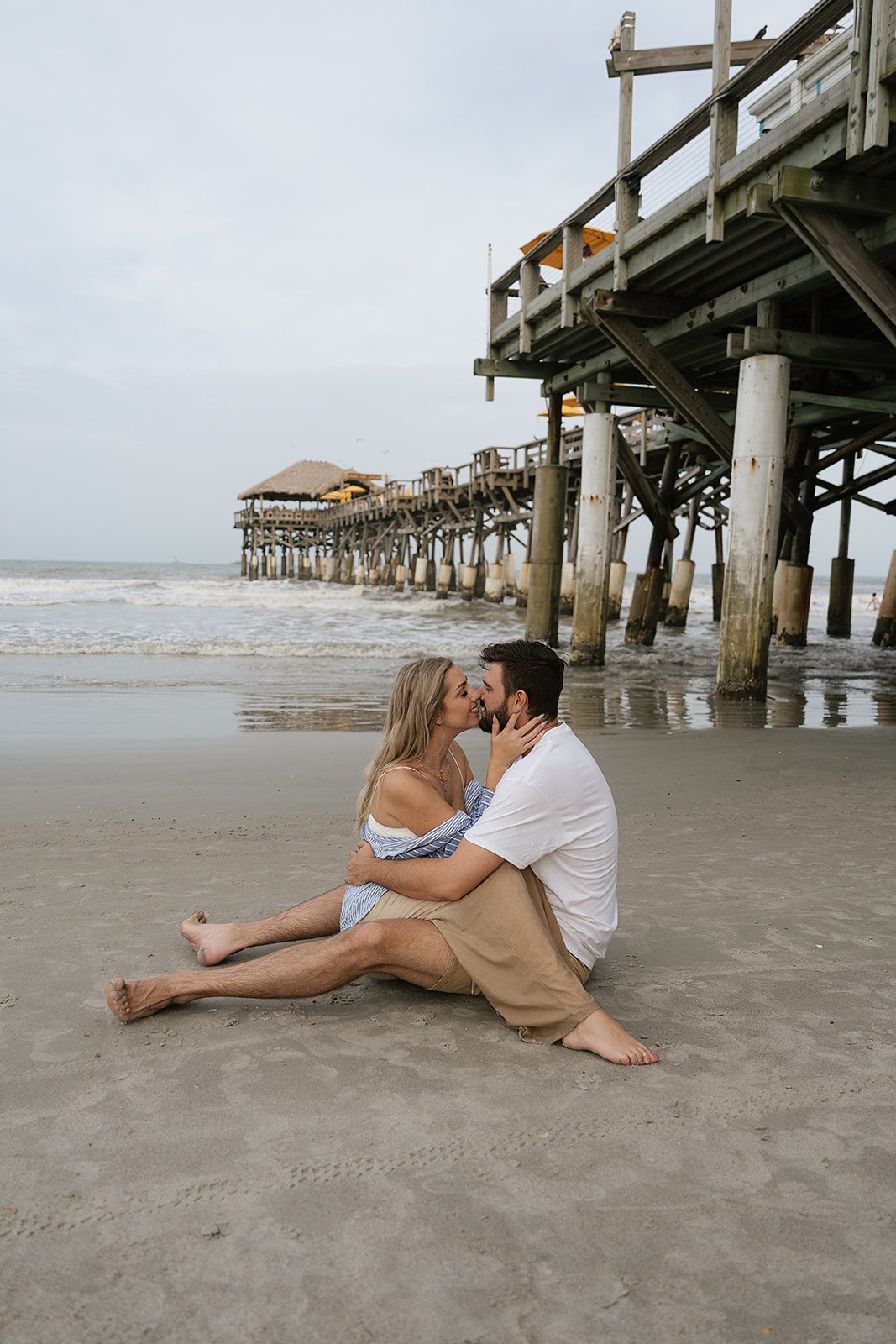 Couple sitting together on the beach beside Cocoa Beach Pier during a romantic Florida couples session